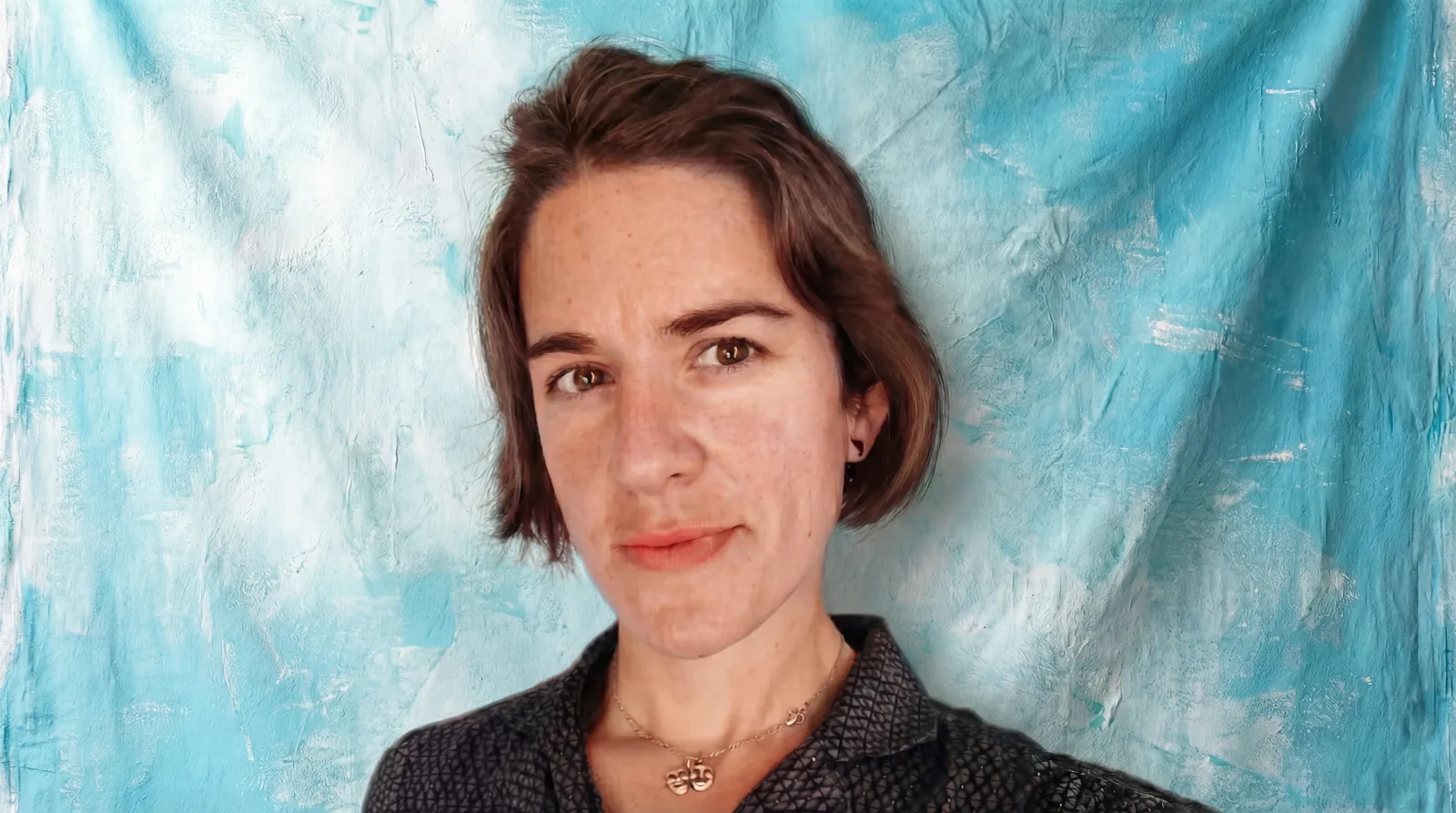 Cass Landrum, Project Manager at Blu Frame and former outdoor educator, looking into the camera against a turquoise backdrop.