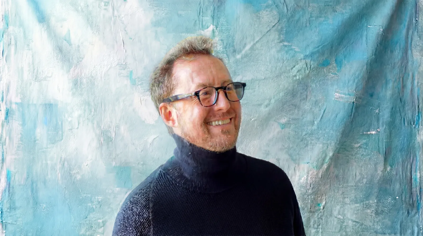 Christopher Webster, Product Owner and Co-Founder of Blu Frame, smiling in glasses against a turquoise studio backdrop.