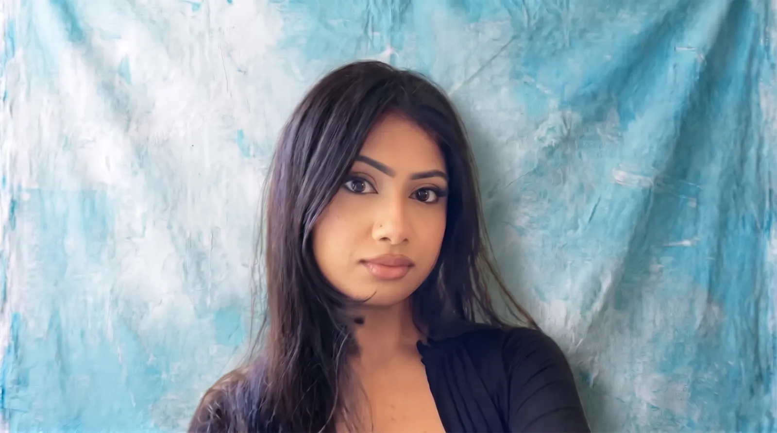Portrait of Faizah Khan, Business Development Specialist, wearing a black top against a textured turquoise and white canvas backdrop
