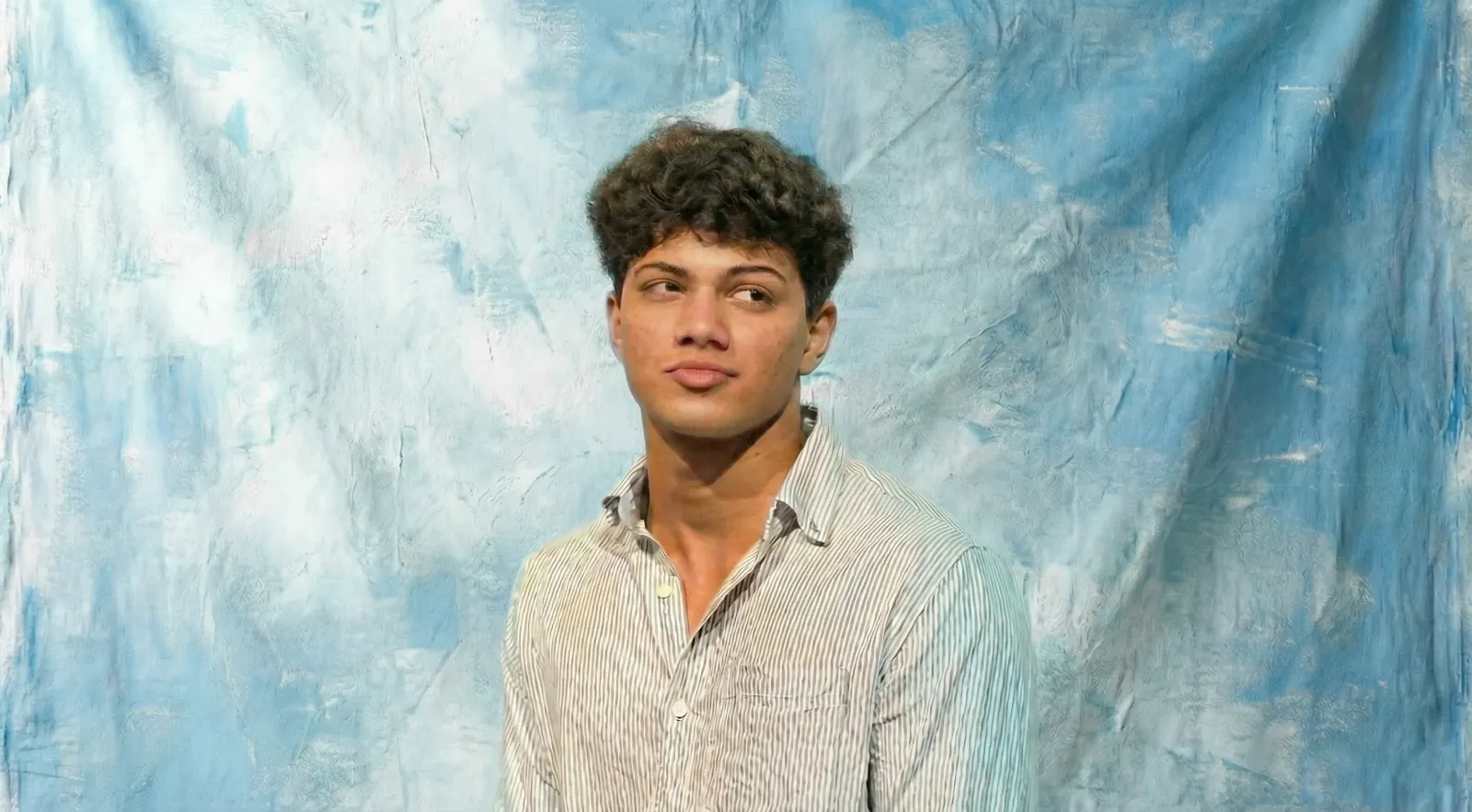 Muhammad Ali, Tech Sales Specialist, wearing a light striped shirt and looking to the side against a textured blue background.